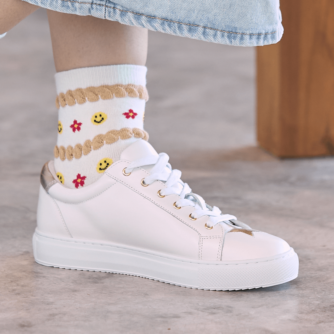 White leather trainer worn by a women with fun socks, but Cocorose London