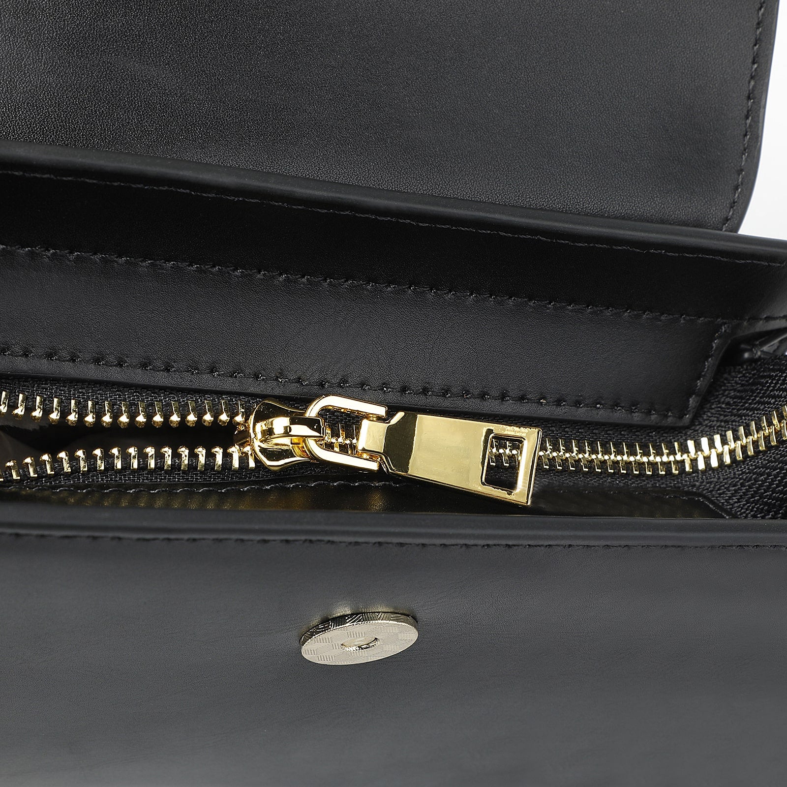 Close-up of a black leather bag with a gold zipper on a white background