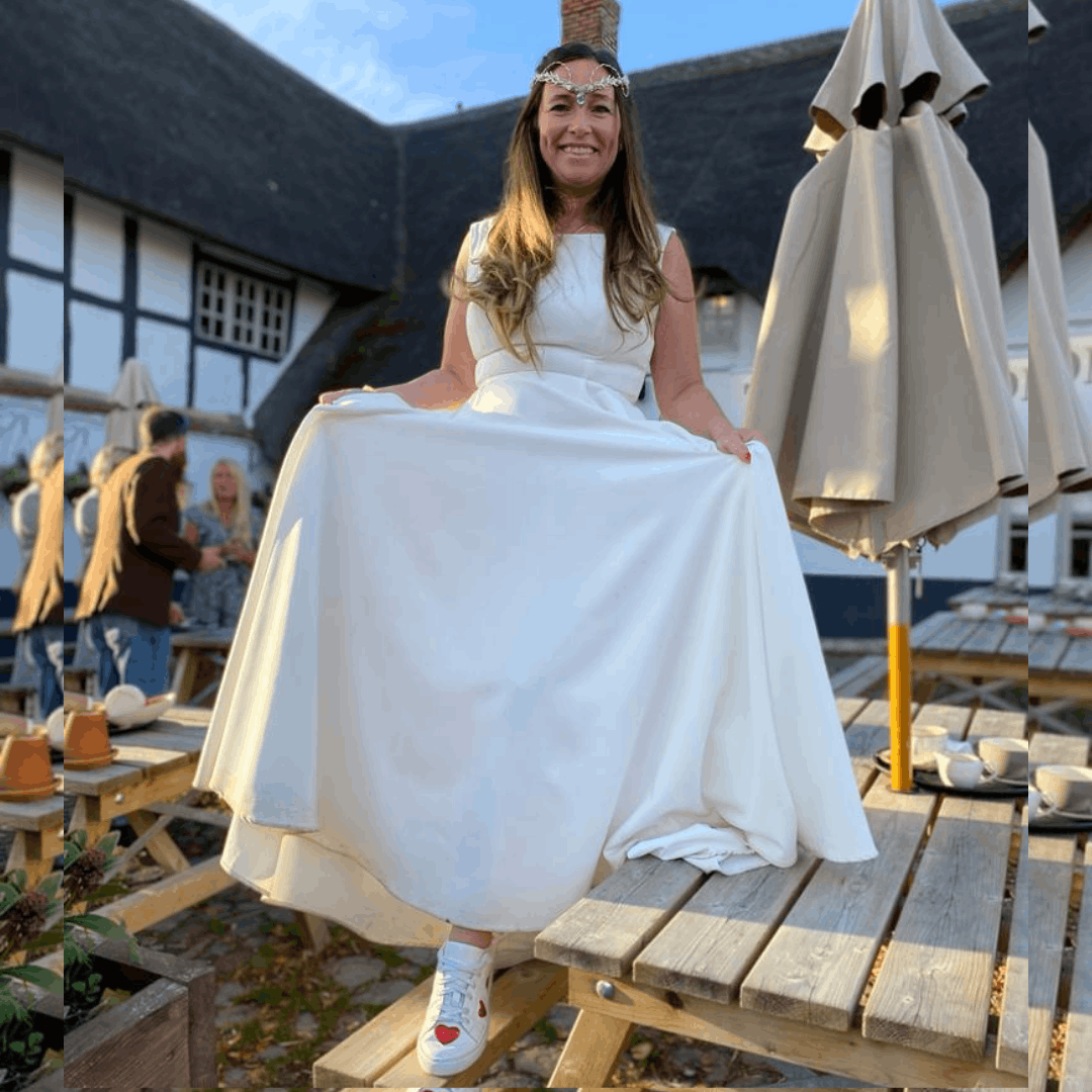 A smiling bride outdoors wearing an A-line wedding dress paired with white leather sneakers featuring red heart accents.