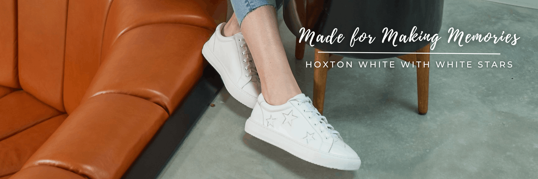 A wide homepage banner showing a close-up of a person sitting by an orange leather couch, wearing white Hoxton sneakers with star details alongside the text, "Made for Making Memories | Hoxton White with White Stars."