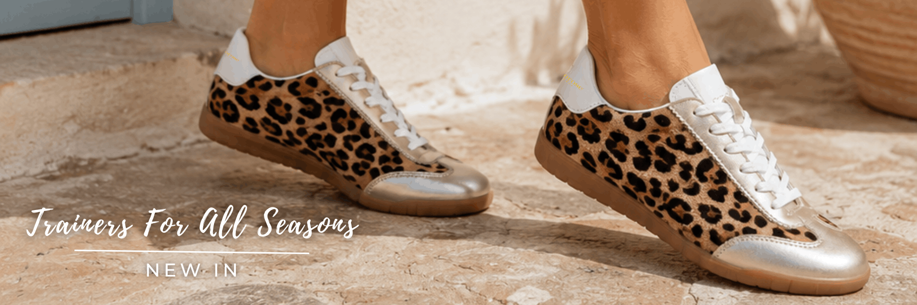 Close-up of leopard print leather trainers with gold accents on a stone path, with text reading "Trainers For All Seasons - NEW IN"