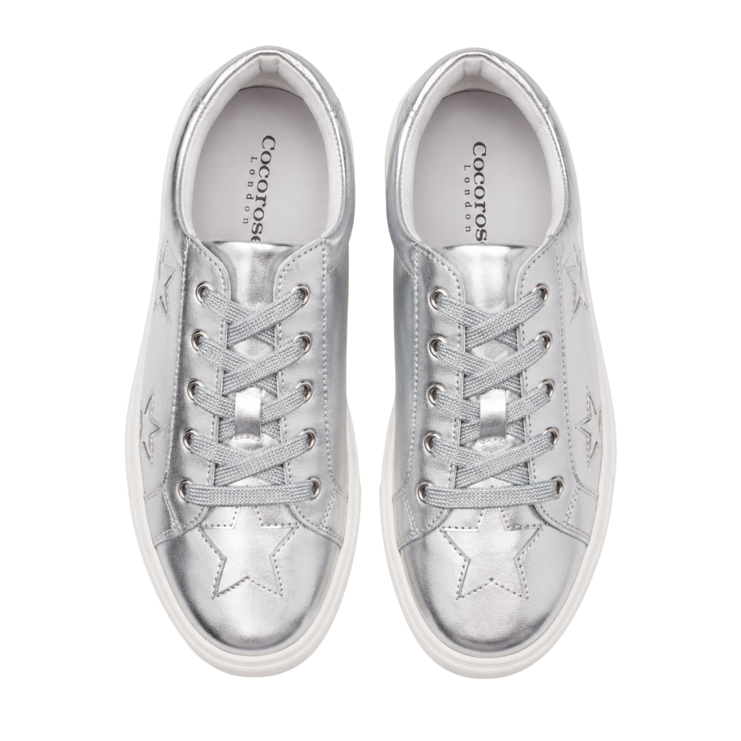 A top-down, bird's-eye view displays a pair of metallic silver leather Cocorose London Hoxton trainers with silver glittery laces and star detailing on the toe boxes.
