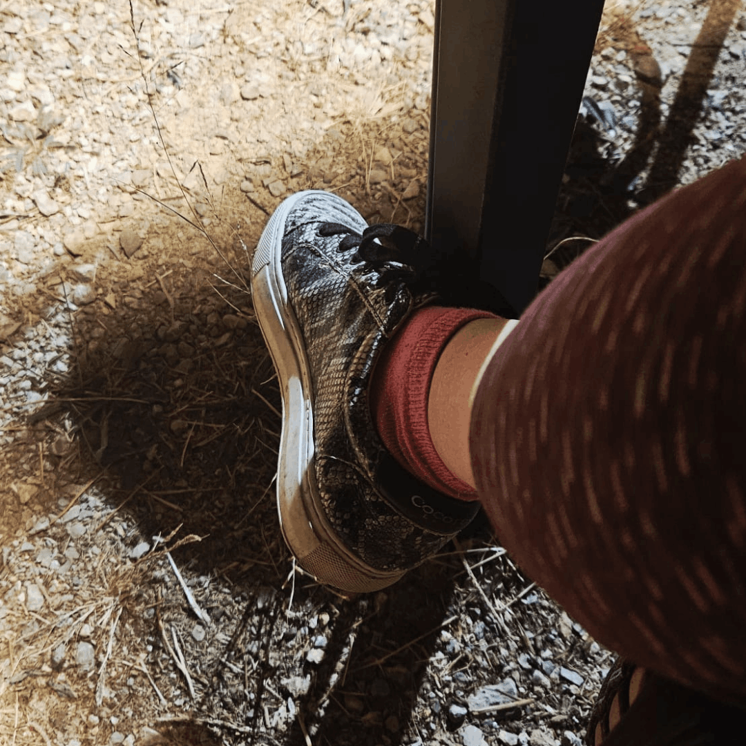 Woman in a black-and-white striped top, beige skirt, and white leather sneakers standing on a paved outdoor plaza near a Ferris wheel and modern sculpture.