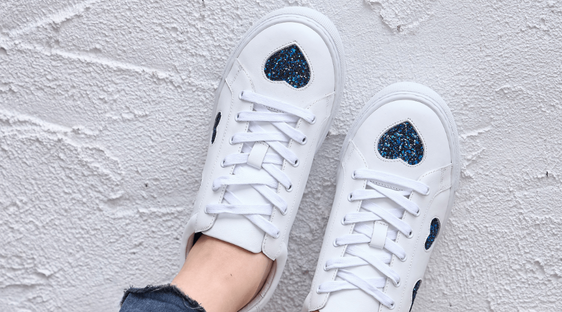 White sneakers with blue heart designs on a light gray textured background