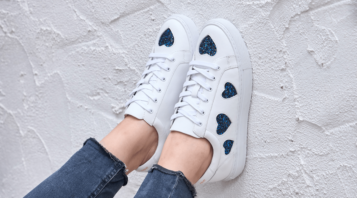 White sneakers with blue heart designs on a light gray textured background