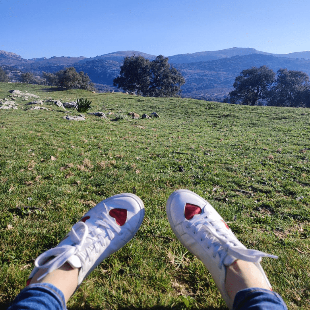 A pair of Cocorose trainers with red hearts on the toe, worn on a hot summers day, with a great view