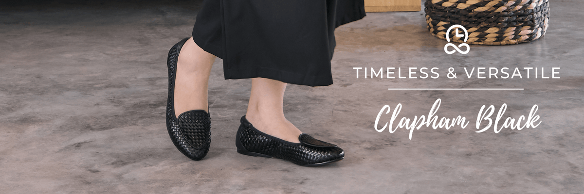 Black leather ballet flats worn by lady in black dress to ankle, walking on stone floor.