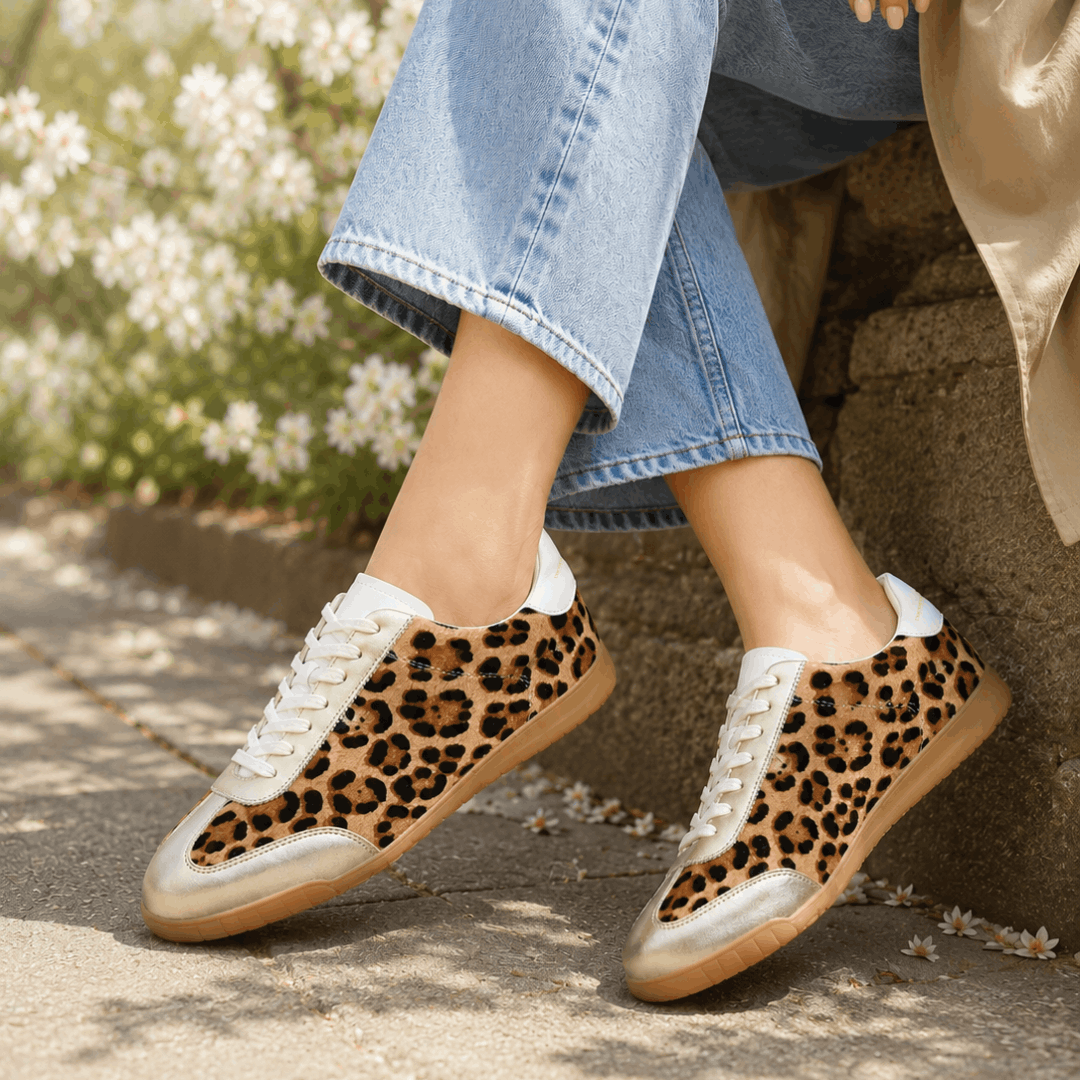 Gold trim trainers with leopard print worn with croped light blue jeans, by girl say on wall with white flowers behind