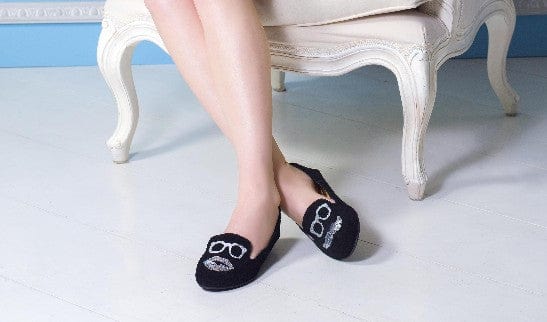 Black soft loafers with embroidered sunglasses and lips, worn by a girl on a throne chair and designed by Cocorose London
