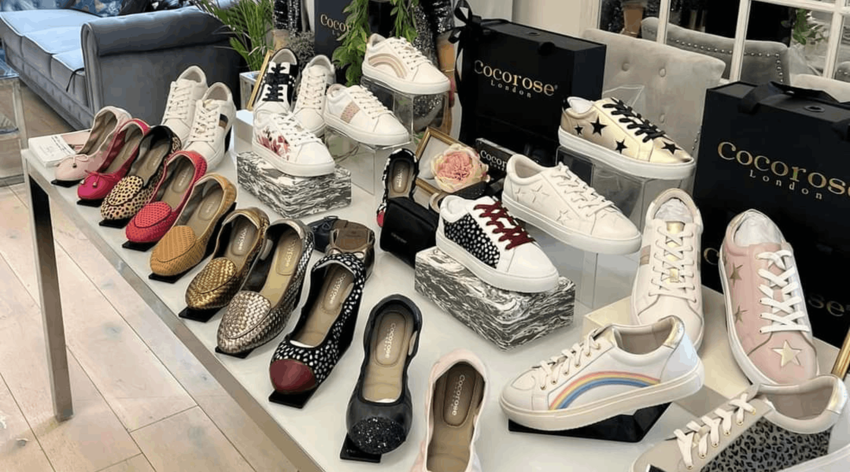 A table display showcasing an array of Cocorose London leather trainers, ballet flats, and loafers alongside branded shopping bags.
