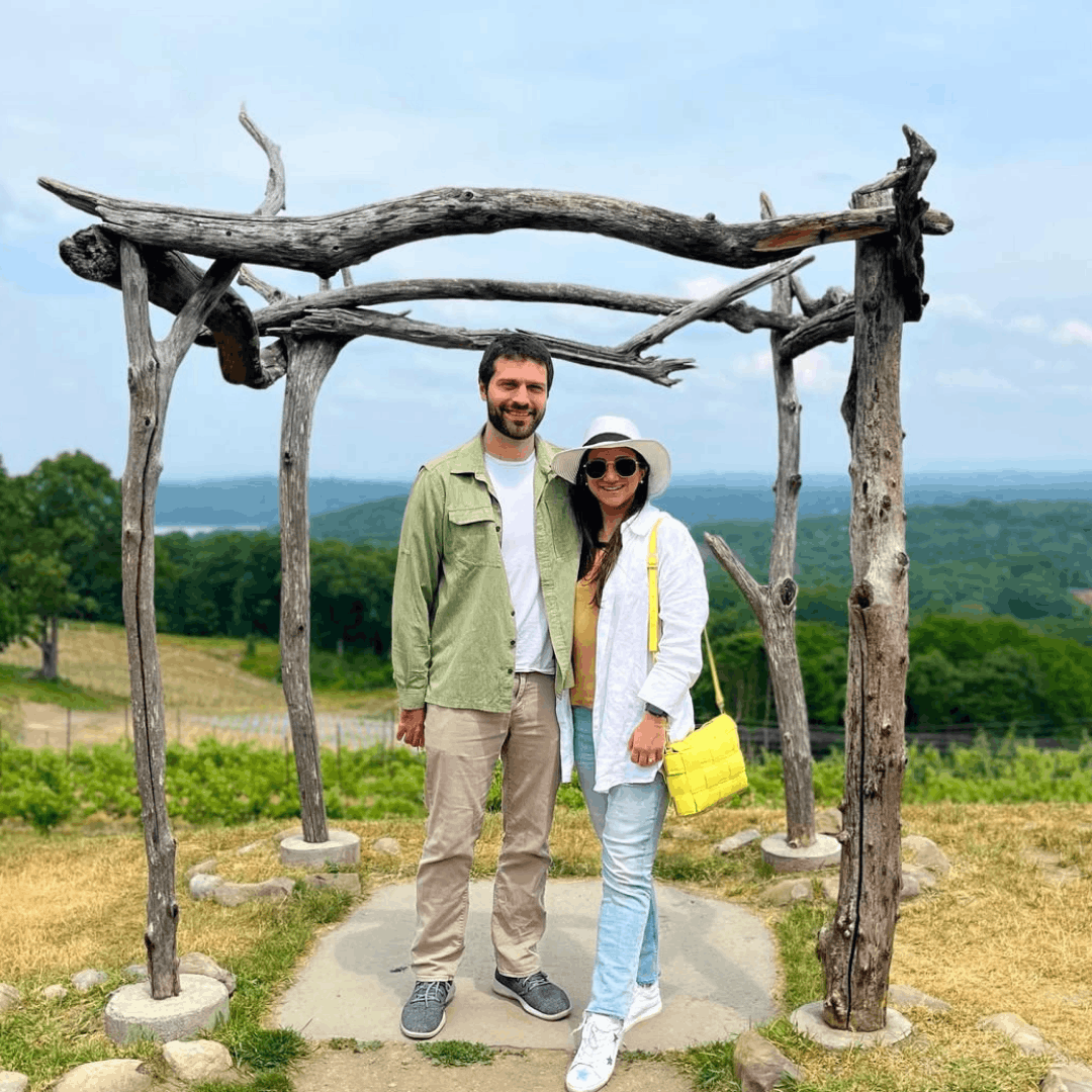 A couple posing together outdoors under a wooden archway, with the woman wearing white sneakers featuring star accents.
