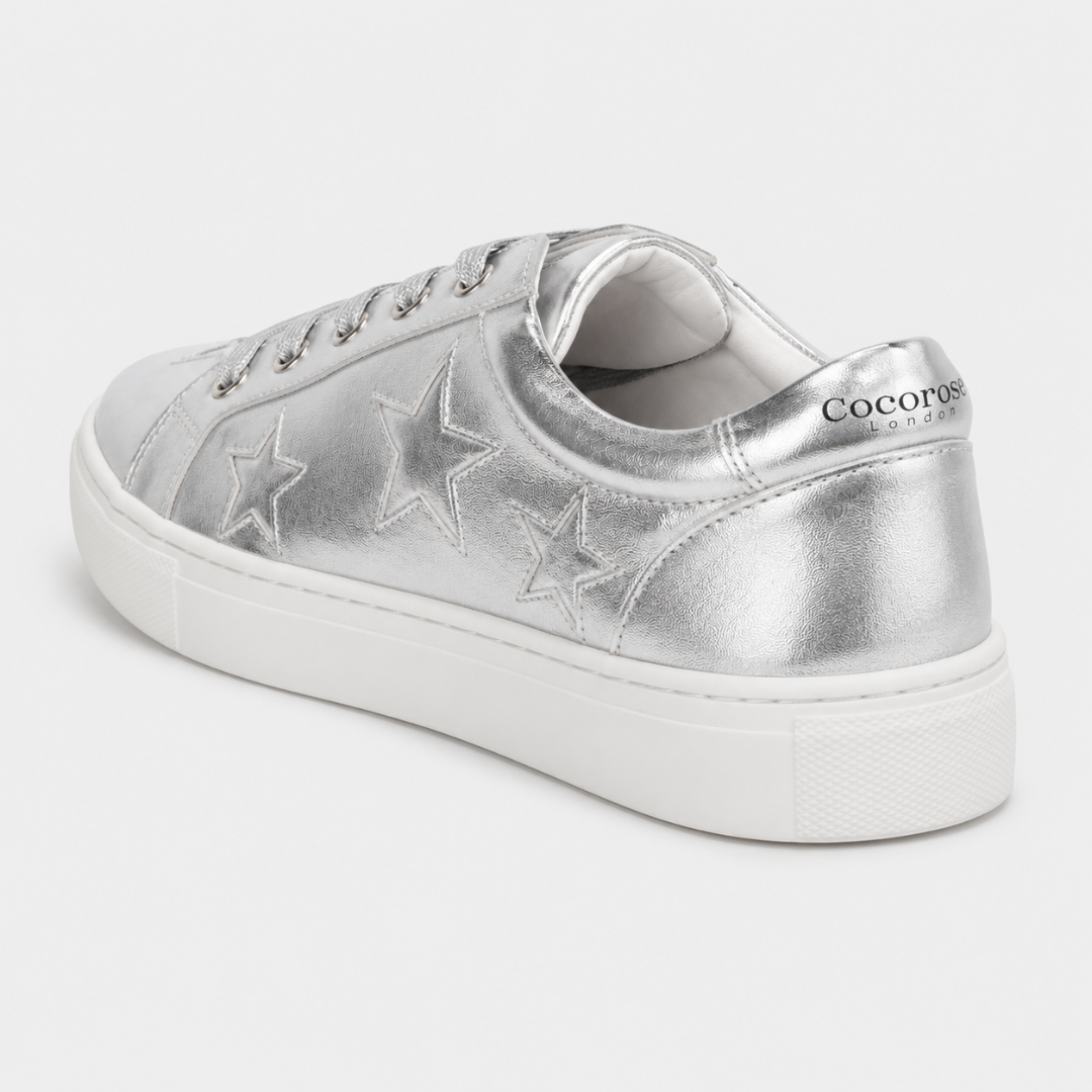 A three-quarter back view of a metallic silver leather Cocorose London Hoxton trainer on a white background, showcasing embroidered stars along the side and the brand name printed on the heel tab.