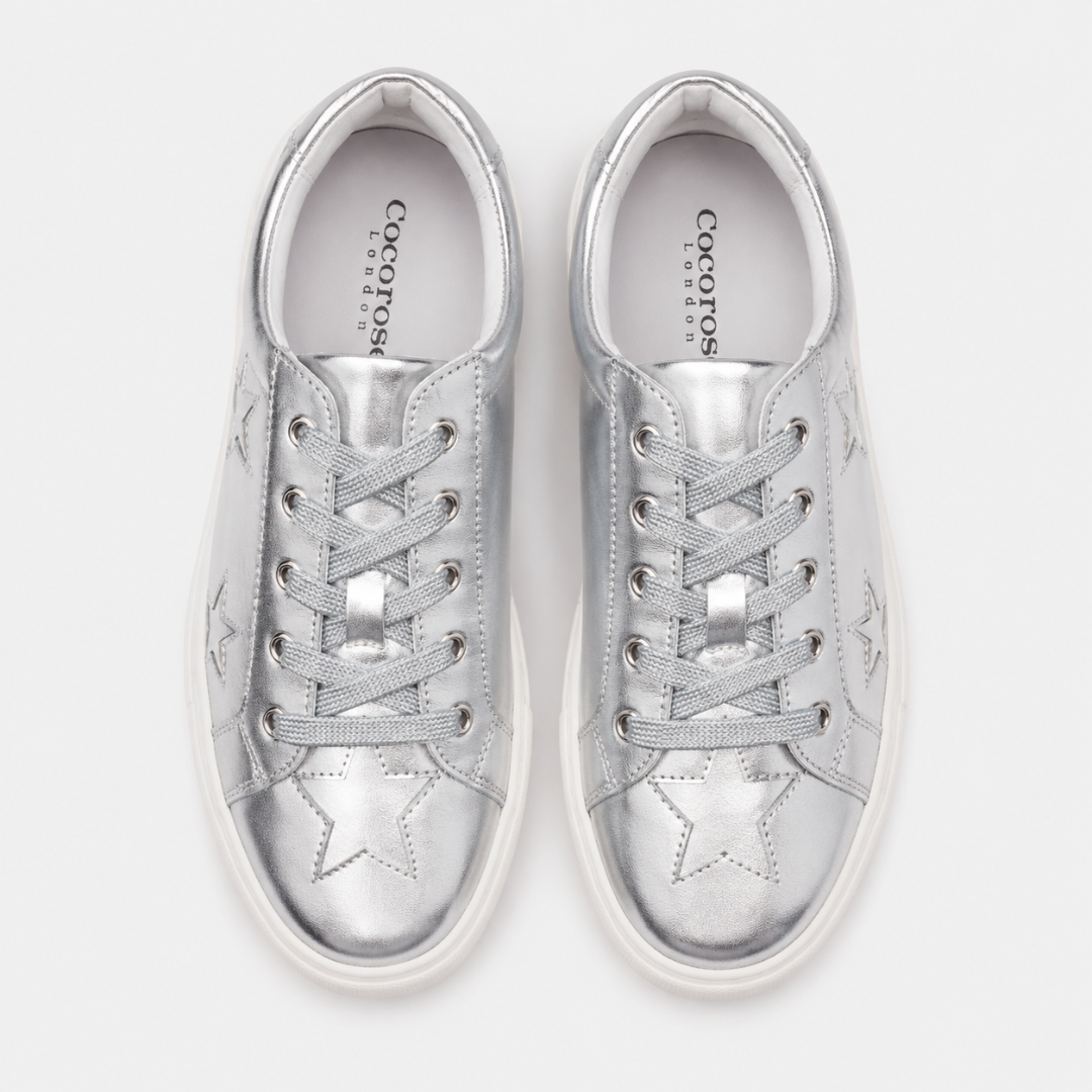 A top-down, bird's-eye view displays a pair of metallic silver leather Cocorose London Hoxton trainers with silver glittery laces and star detailing on the toe boxes.