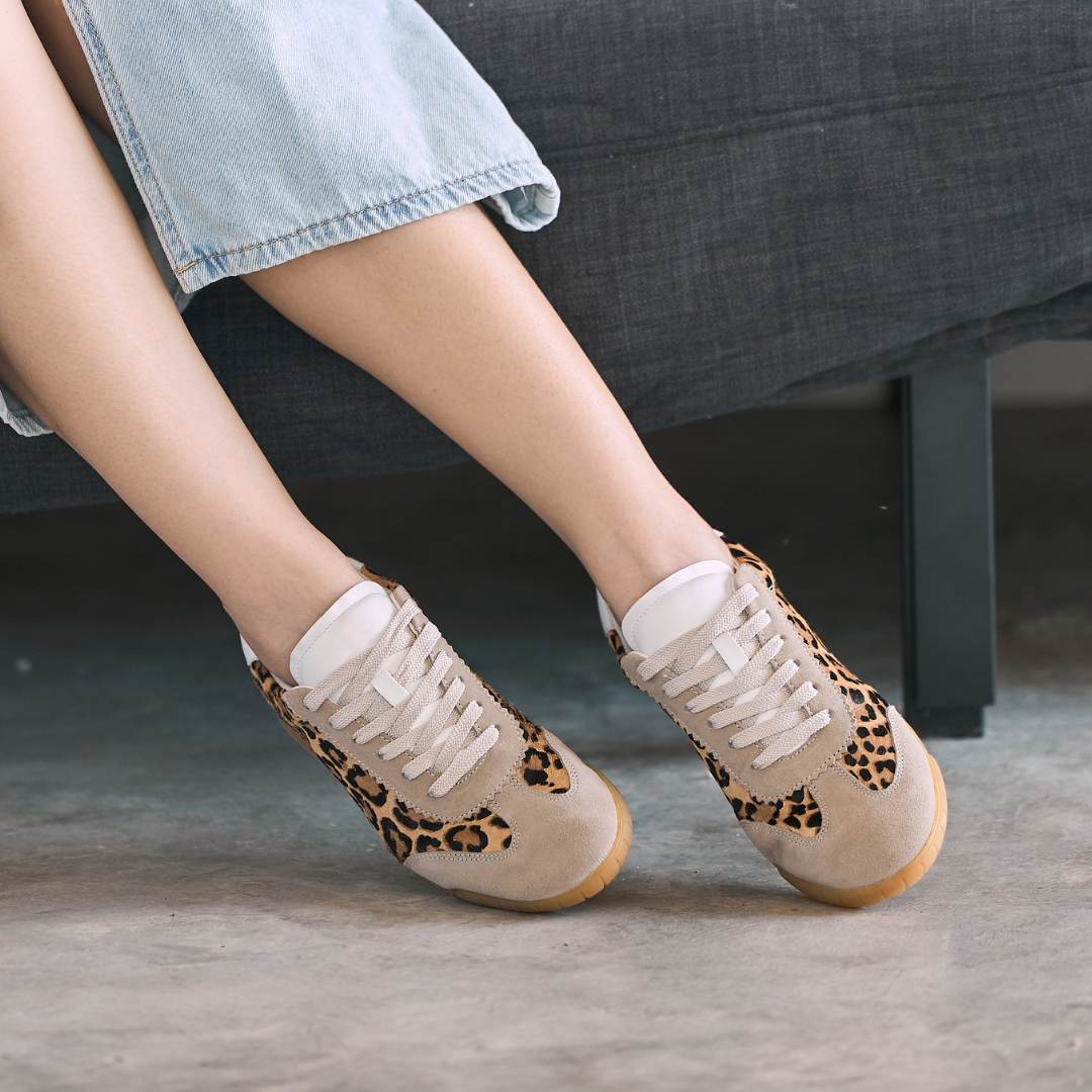 Beige sneakers with leopard print details worn by a person sitting on a grey couch.