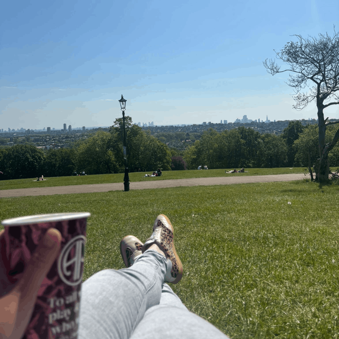 Relaxing on a sunny day in a grassy park overlooking a city skyline while wearing leopard print sneakers and holding a coffee cup.