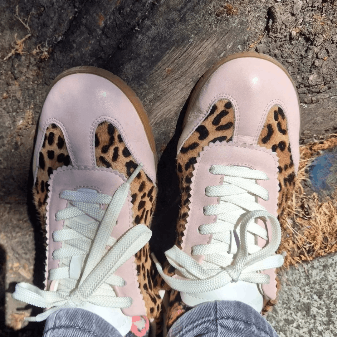 A top-down view of pink leather trainers with textured leopard print paneling and white laces.