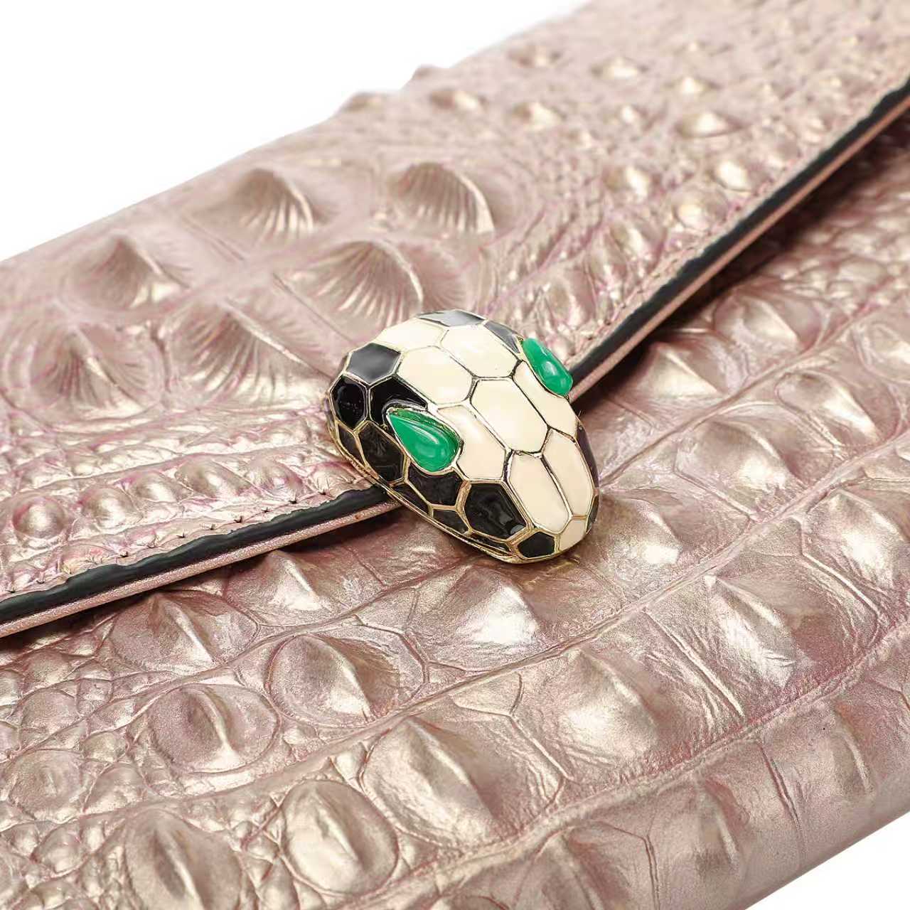 Rose gold clutch with snake head design and green eyes on a white background