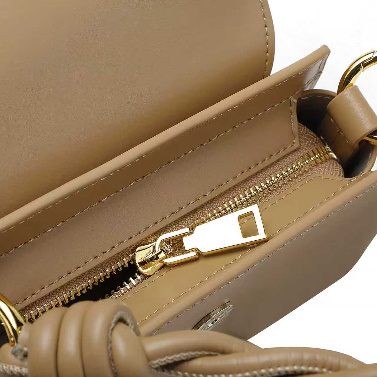 Close-up of a beige handbag with a gold zipper and handle.