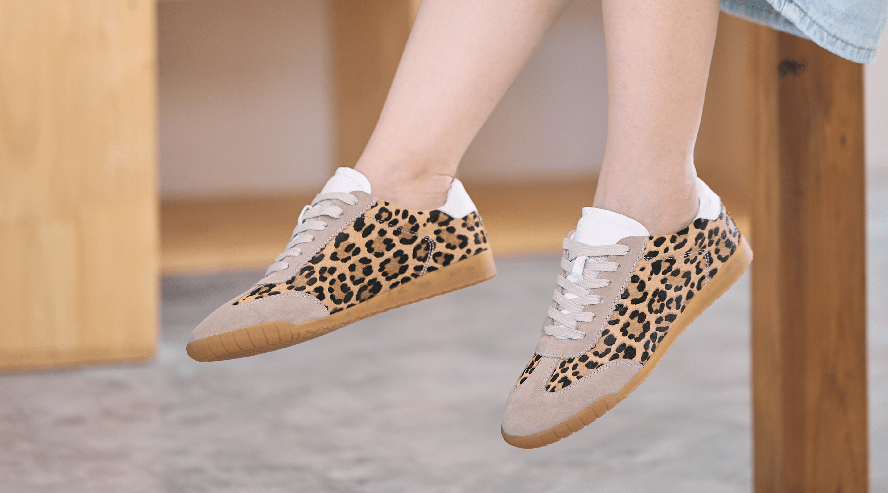 Leopard print sneakers with white laces worn by a person sitting on a wooden bench.