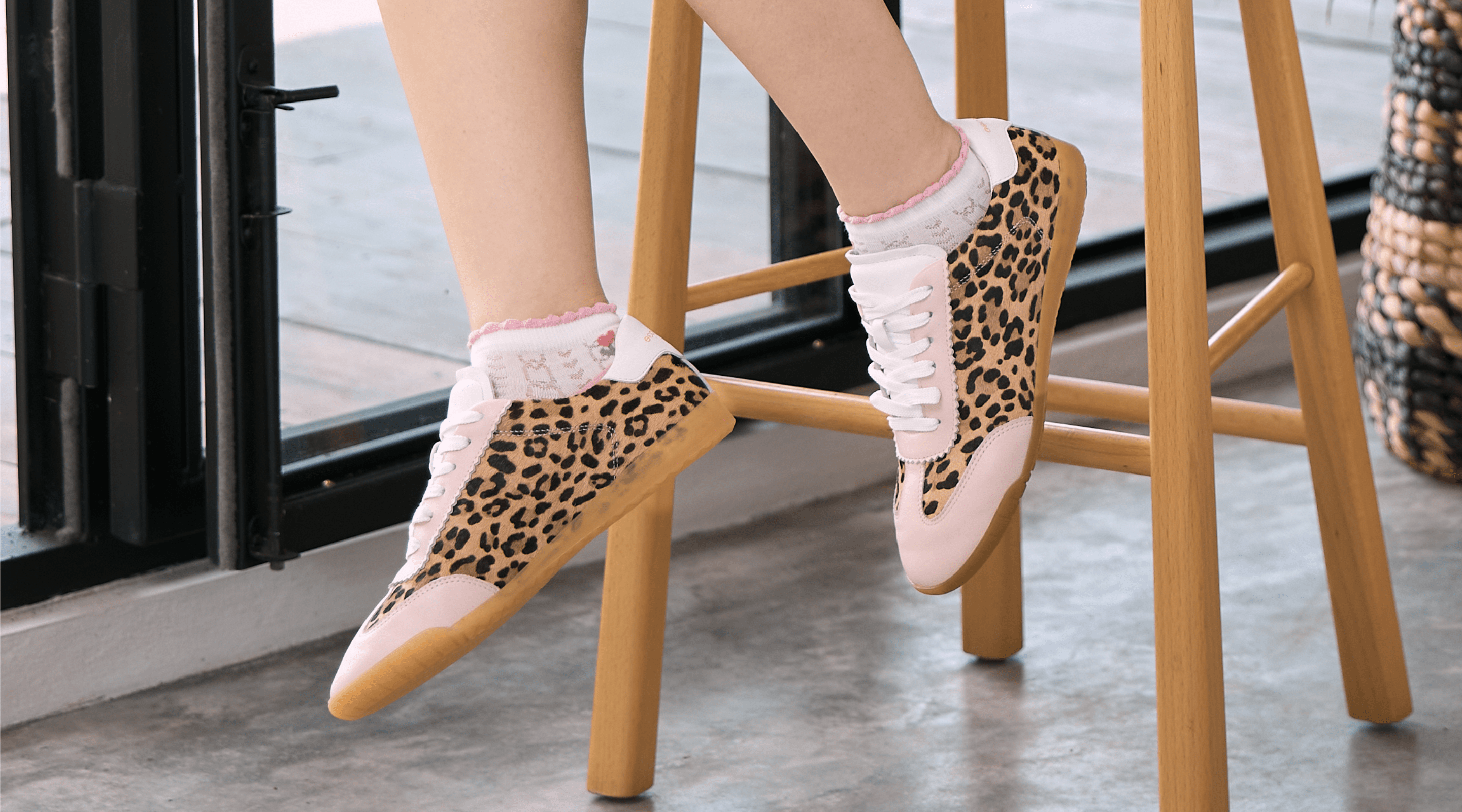 Person wearing leopard print trainers, with pink trim, and white socks on a wooden stool