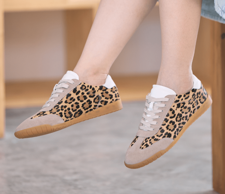 Leopard print women's trainers worn by a lady, on a stool, half body image